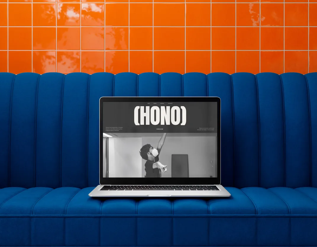 Portátil sobre un sofá azul mostrando la web HONO