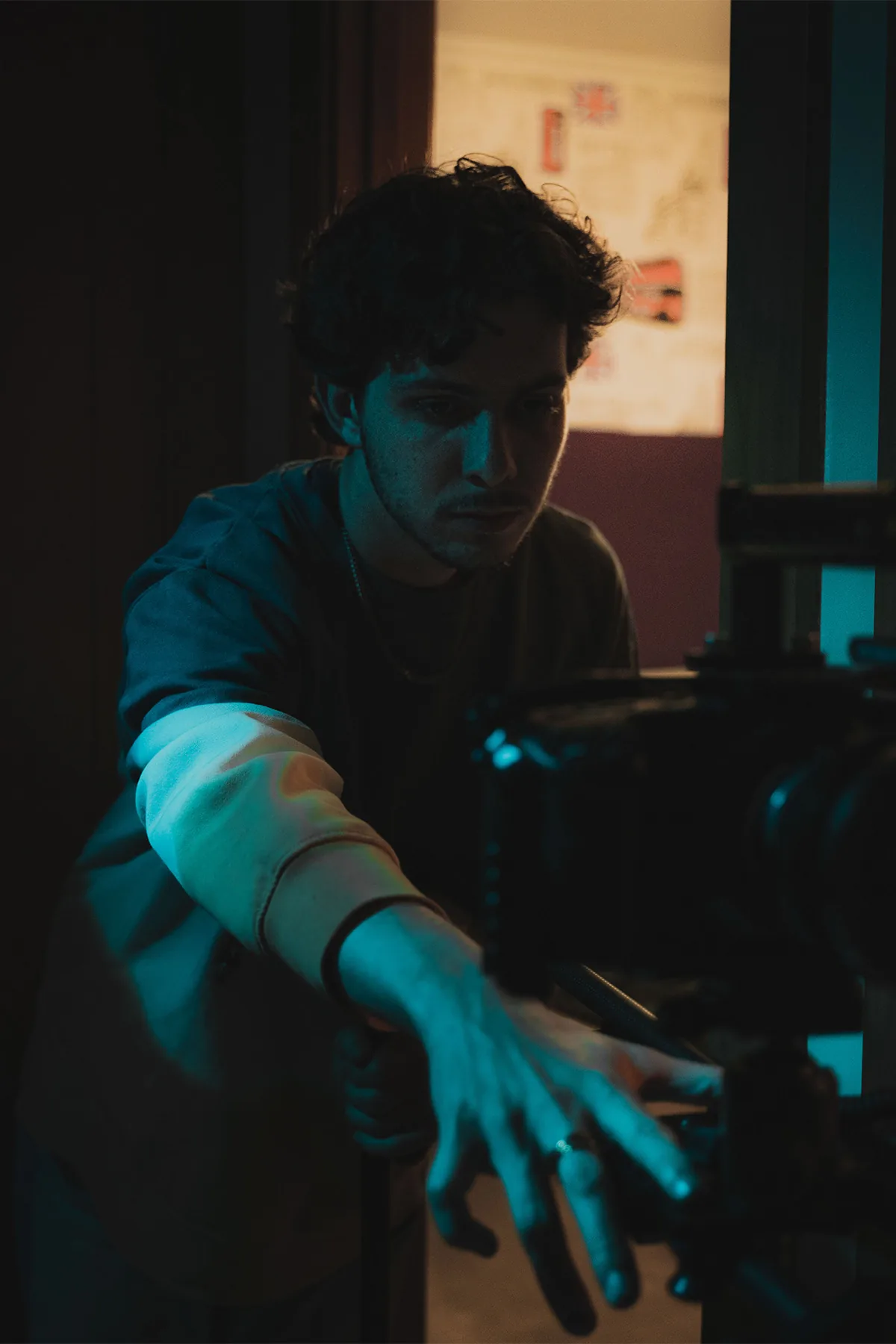 Retrato de un joven con luz turquesa moviendo una cámara de cine en una habitación oscura