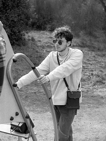 Retrato en blanco y negro de un joven con gafas de sol junto a una estructura de juegos