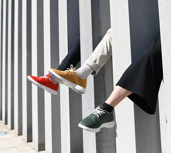 Piernas con zapatos de colores asomando junto a un muro de rayas verticales